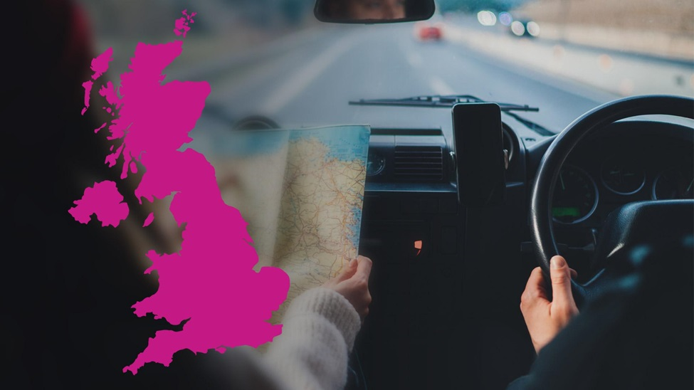 A pink map of the UK is overlaid a photo of people driving down a road with the passenger reading from a map